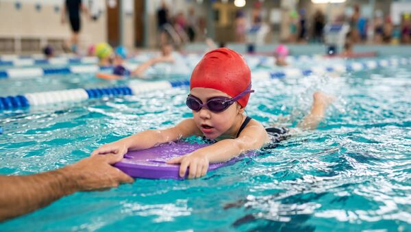 A young girl practices swimming with a kickboard gaining confidence in the water during a fun lesson.
